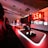 A modern gaming setup featuring several high-end computers with illuminated red interior lighting. The room is equipped with gaming chairs exhibiting a sleek black and red design. Multiple monitors are arranged on a long desk, and peripheral devices like keyboards and mice are uniformly placed, reflecting an ambiance ideal for gaming or competitive play.